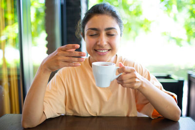 Mid adult woman holding coffee while sitting on table