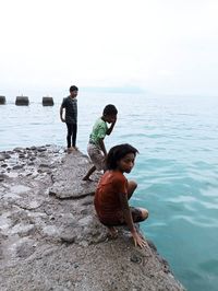 Rear view of boys on rock by sea against sky