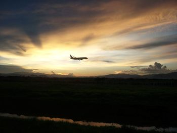 Silhouette bird flying over landscape against sunset sky