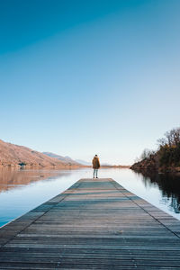 Rear view of man walking on boardwalk against clear sky