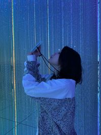 Side view of woman standing against blue wall