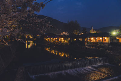 Illuminated buildings by river against sky at night