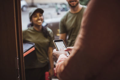 Midsection of male customer using smart phone with technicians at doorway