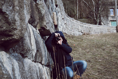 Woman photographing while crouching by retaining wall