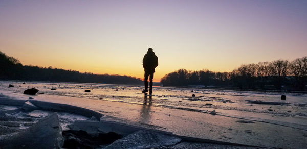 Silhouette man standing on snow covered land against sky during sunset