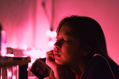 Close-up of young woman with eyes closed lying against pink light at home