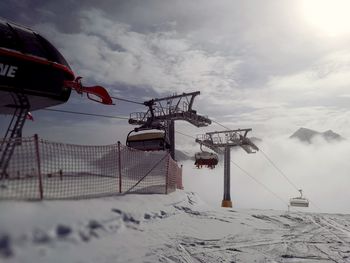 Low angle view of overhead cable cars against cloudy sky during winter