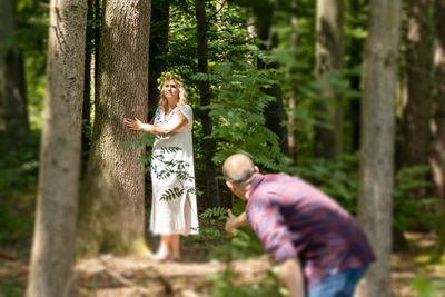 Woman standing by tree trunk in forest