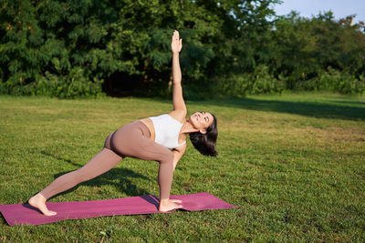 Full length of young woman exercising on field