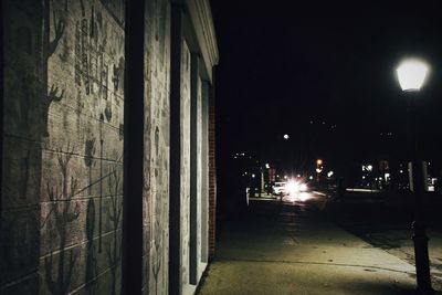 Illuminated street light on sidewalk by building at night