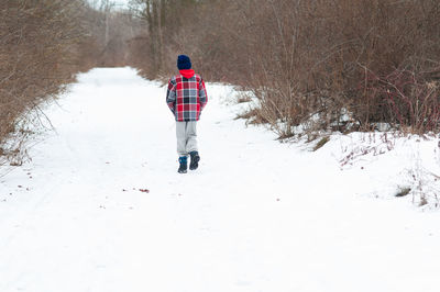 Rear view of boy walking on snow covered landscape