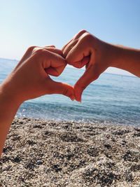 Cropped hands of women making heart shape against sea and sky