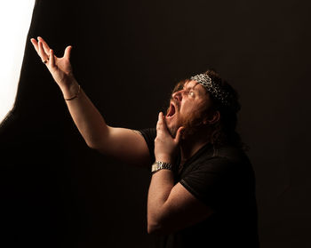 Side view of young man looking away against black background