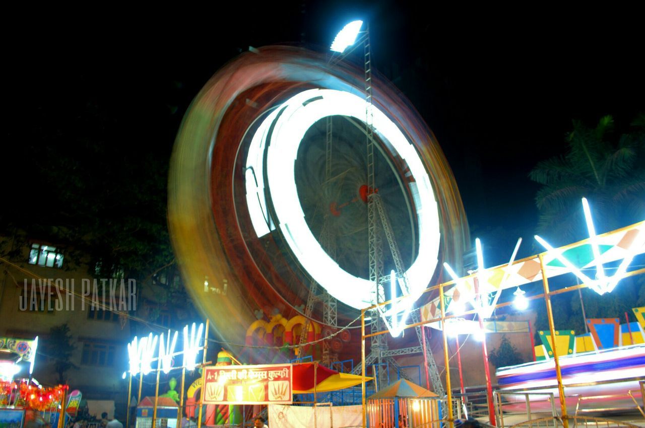 illuminated, night, built structure, architecture, low angle view, building exterior, circle, amusement park, arts culture and entertainment, ferris wheel, sky, amusement park ride, clear sky, lighting equipment, outdoors, no people, tree, blue, city, street light