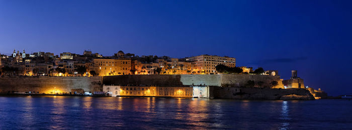 Illuminated buildings against blue sky at night