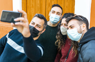 Cheerful friends doing selfie while standing against wooden wall