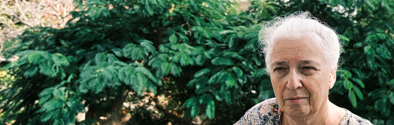 Portrait of an elderly woman with gray hair on a background of greenery. copy space.