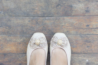 Low section of woman wearing shoes standing on wooden floorboard