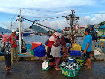 Rear view of people working on boat against sky