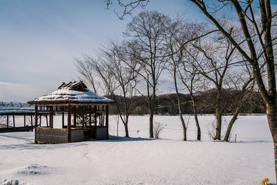 House and bare trees on snow covered landscape against sky