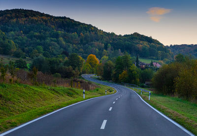 Road amidst trees and mountains against sky