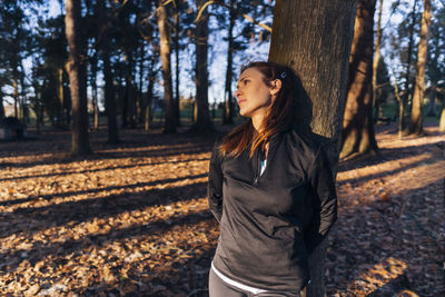 Portrait of teenage girl standing by tree trunk in forest