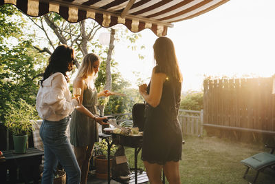 Female friends talking while preparing food on barbecue grill in dinner party