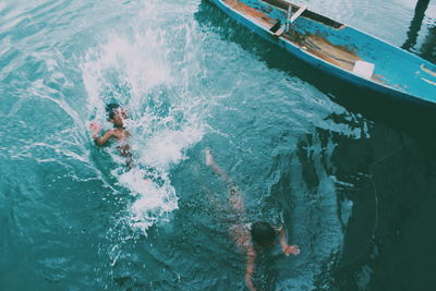 High angle view of boys swimming by boat on lake