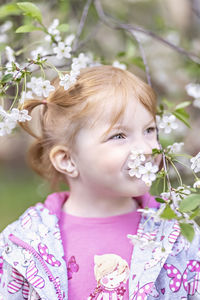 Close-up portrait of a toddler girl with red hair in front of a cherry blossom. spring.