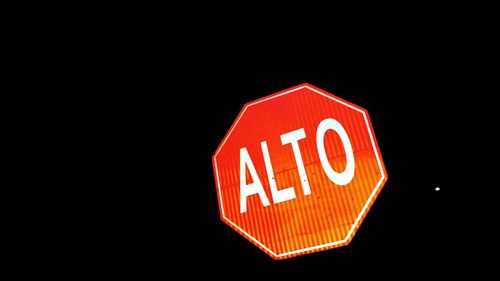 Low angle view of illuminated sign against black background