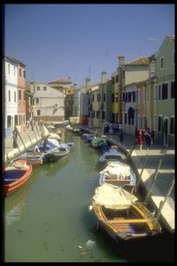 Sailboats moored on canal by buildings in city against clear sky