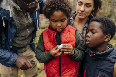 Son examining animal shell with family during vacation in forest