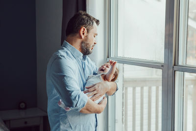 Side view of man playing with daughter while holding by window