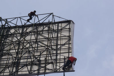 Low angle view of men working on billboard against sky