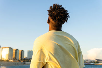 Back view of unrecognizable of calm african american male in casual clothes standing with closed eyes on street in summer