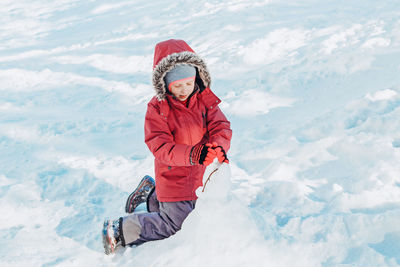  girl child in warm clothes playing with snow in park outside. kids outdoor seasonal activity.