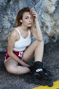 Portrait of young woman wearing inline skate while sitting against rock