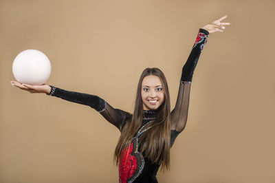 Portrait of smiling young woman with ball dancing against brown background