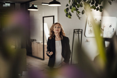 Confident businesswoman with smart phone standing in creative office