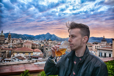 Young man drinking wine against buildings in city