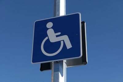 Low angle view of disabled sign on pole against clear sky