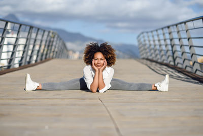 Portrait of smiling young woman against retaining wall against sky