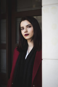 Portrait of beautiful young woman standing by column