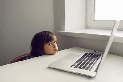 Boy child sits at a table near the window with a laptop and communicates with relatives