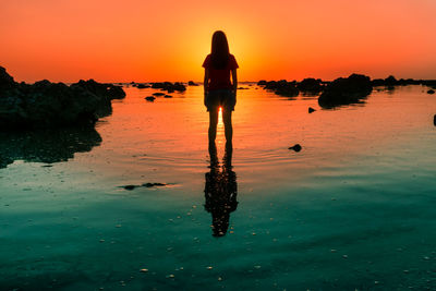 Silhouette man standing in sea against sky during sunset