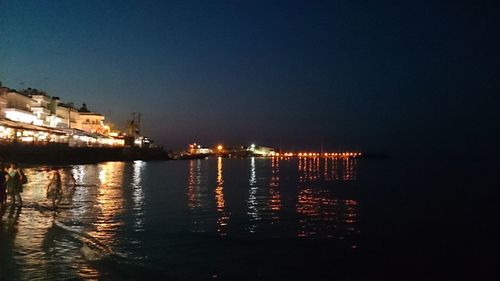 Illuminated city by sea against sky at night