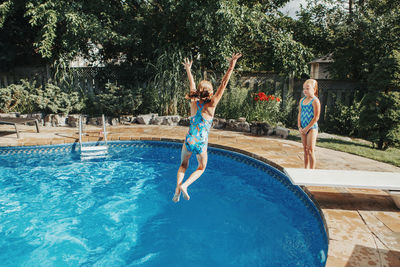 Girl jumping in swimming pool against trees