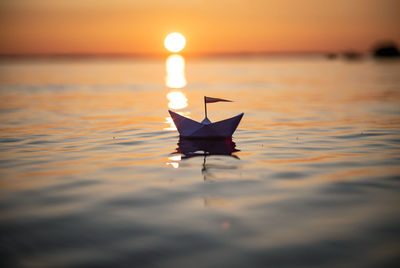 Paper boat floating on sea against sky during sunset