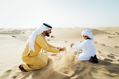 Father and son enjoying while kneeling in desert