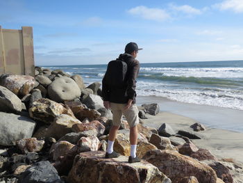 Rear view of woman standing on rock at beach